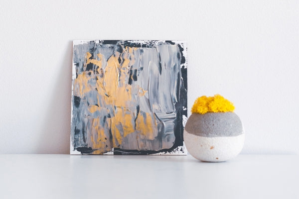 A blue abstract painting with a vase of yellow flowers next to it.