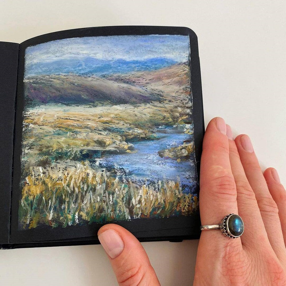 Hand with an opal ring, holds an oil pastel artwork.