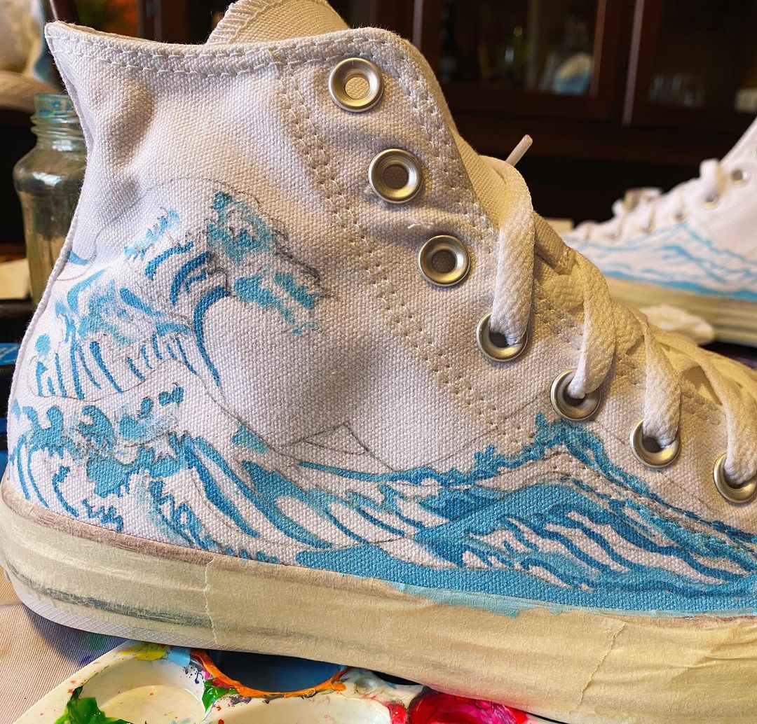 Hokusai's wave painted in blue on a pair of plain white converse sneakers.