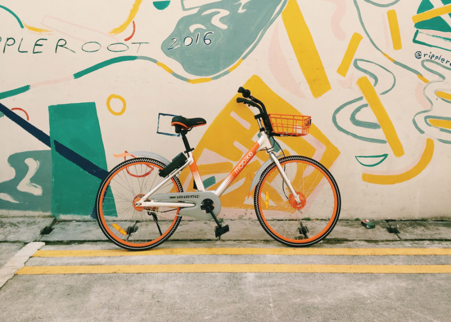 An orange bike next to a yellow abstract painted mural on a city wall.