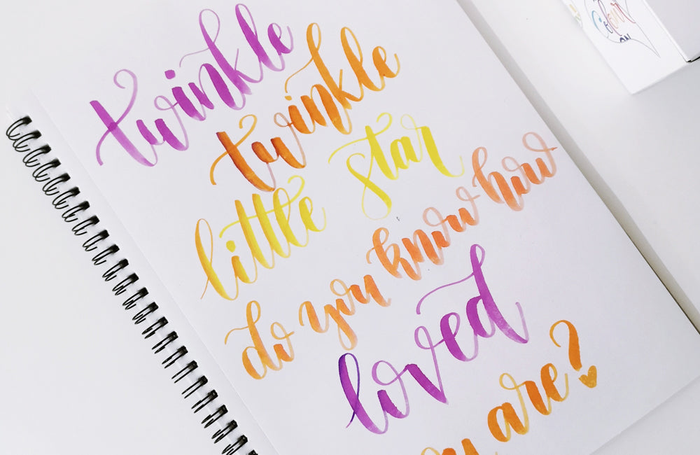 Words Witten in a calligraphy style in bright colours, on a sketchbook.