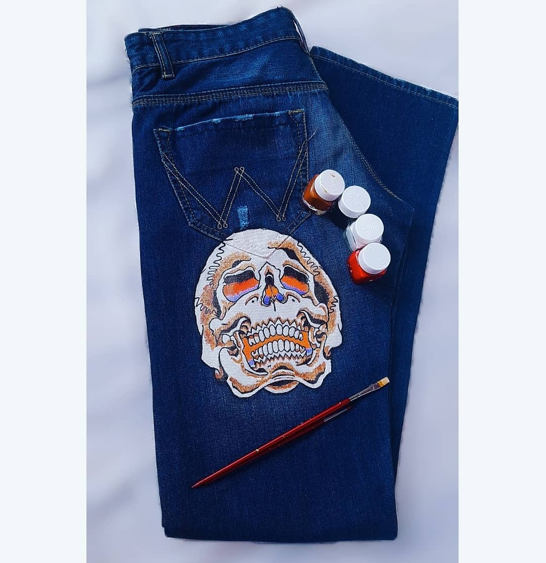 A white skull with orange and purple details painted on a pair of dark blue jeans.