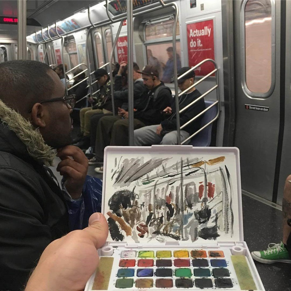 Hand holding a watercolour set with paintings of passengers on the subway in front.
