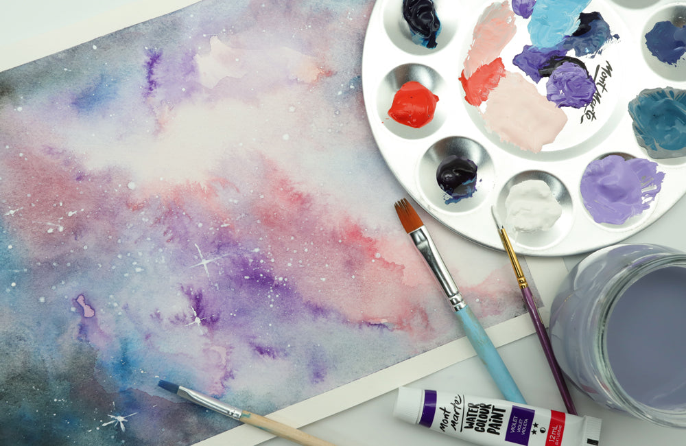 Blue, purple, pink, red and white galaxy painting on a table with a filled colour pallet, brushes and purple water filled jar.
