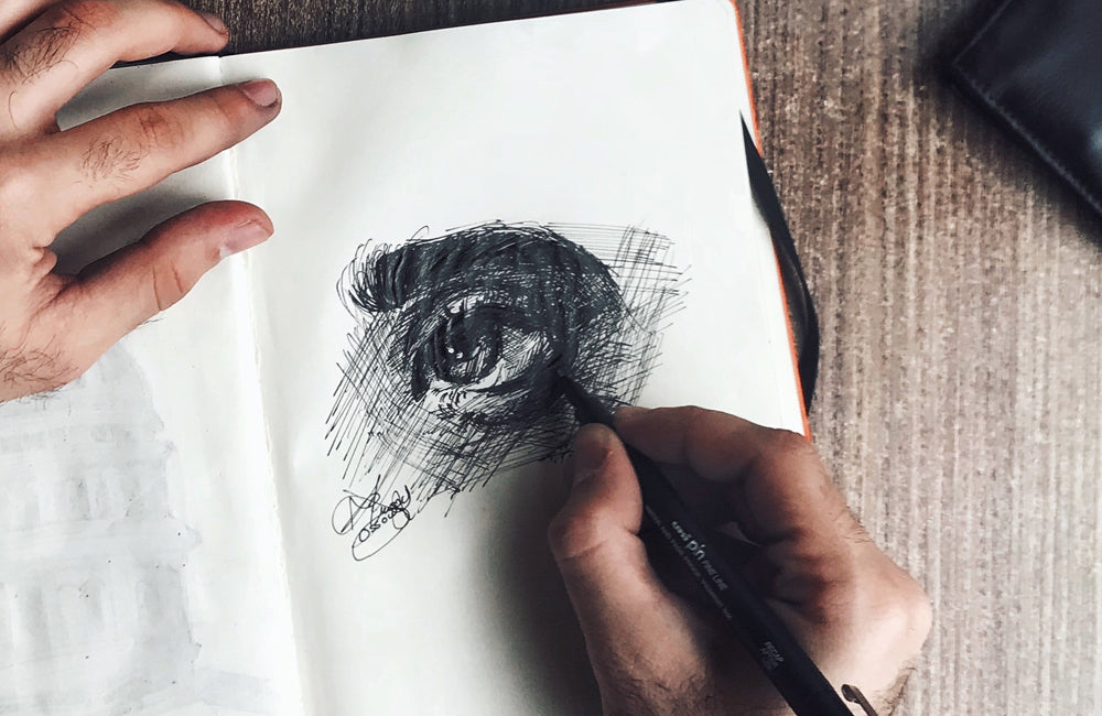 Hand sketching a realistic eye with pen in a notebook.