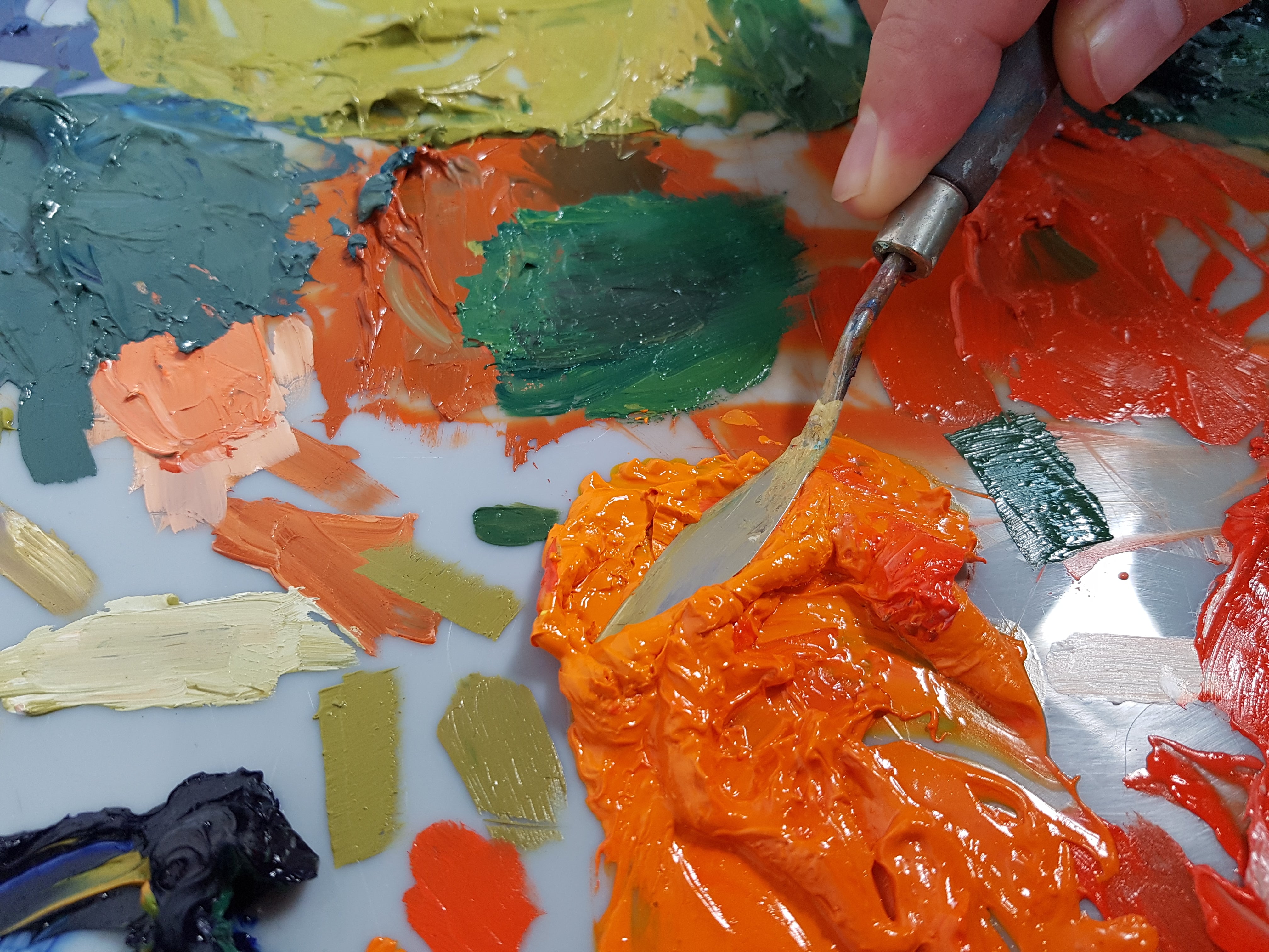 Palette knife squashing orange paint on a messy acrylic palette.
