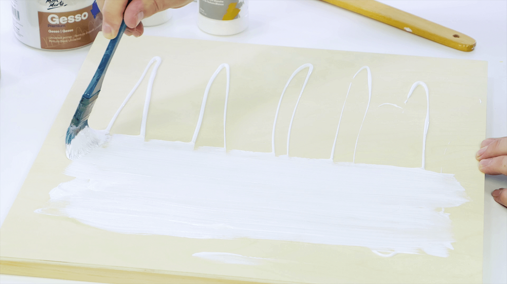 A blue taklon paint brush painting gesso over a wooden board.