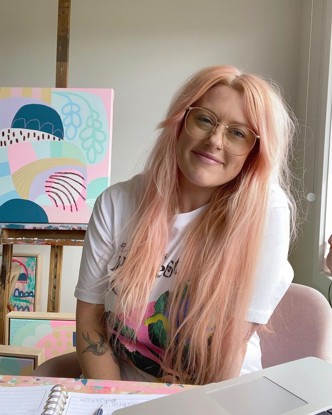 Artist Rach Jackson smiling in her studio with a pastel abstract artwork behind her on an easel.