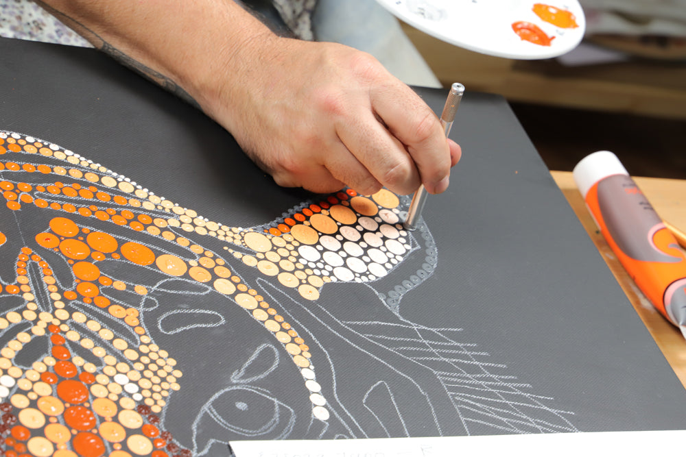 Hand adding paint dots to tiger painting.