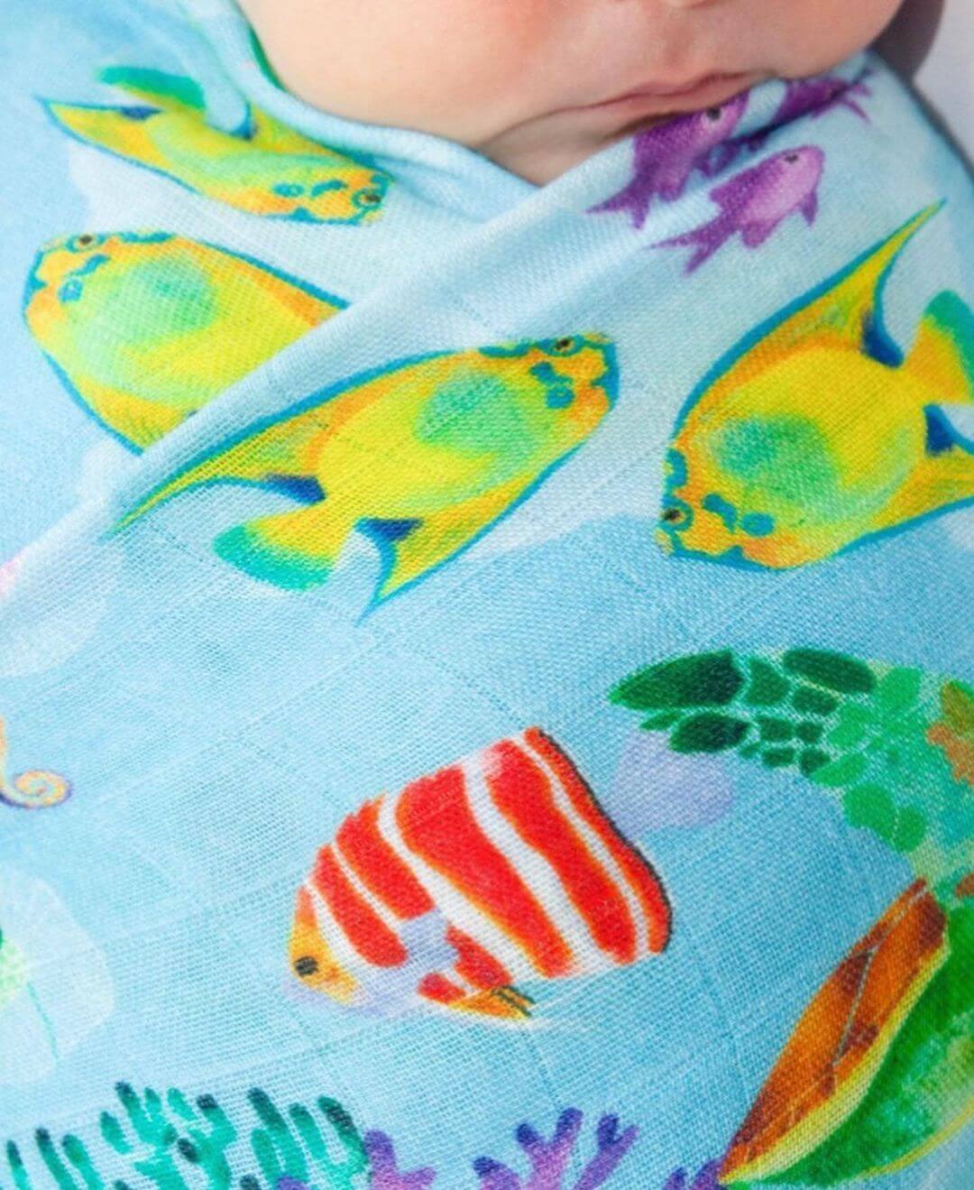 Baby wrapped in blue fabric with tropical fish watercolour painting designed on the fabric.