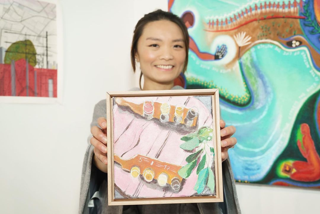 2. Candy holding her artwork in front of her at an exhibition