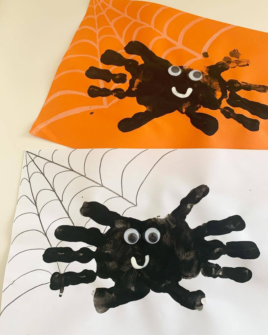 Halloween craft made from orange and white paper with painted a child's handprints made to look like spiders.