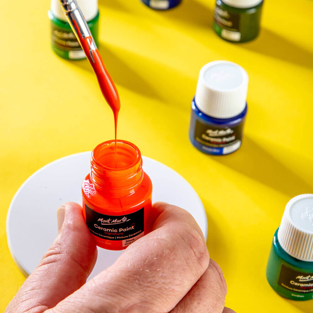 Hand dipping a taklon brush into an orange ceramic paint.