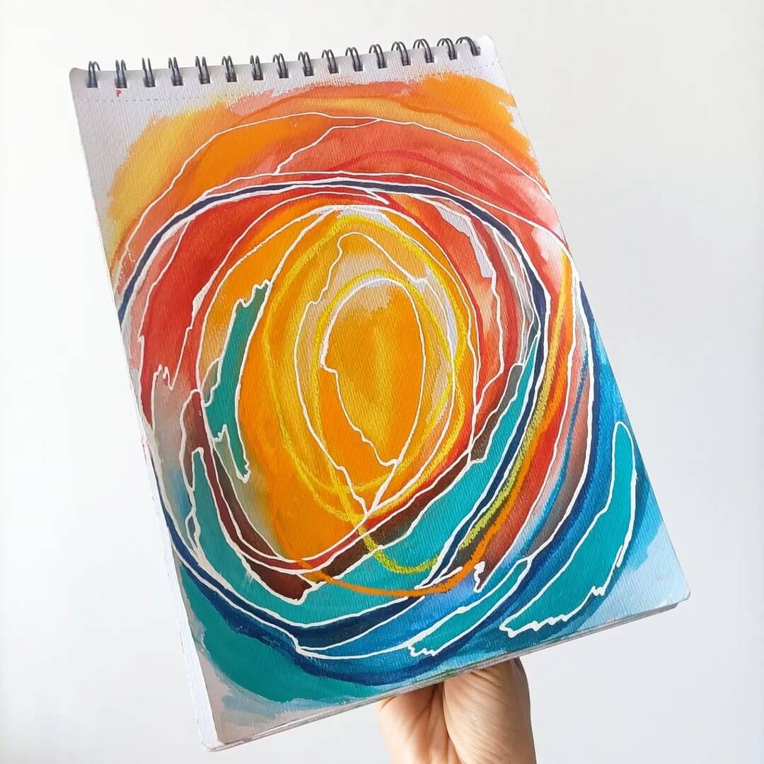 Hand holding a watercolour sketchpad with a bright yellow and blue abstract circle painted on.