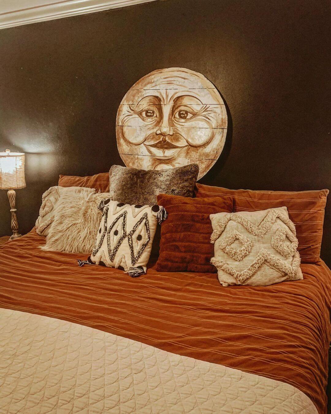 Moon face painted on upcycled wooden boards, hanging on a wall above a bed.