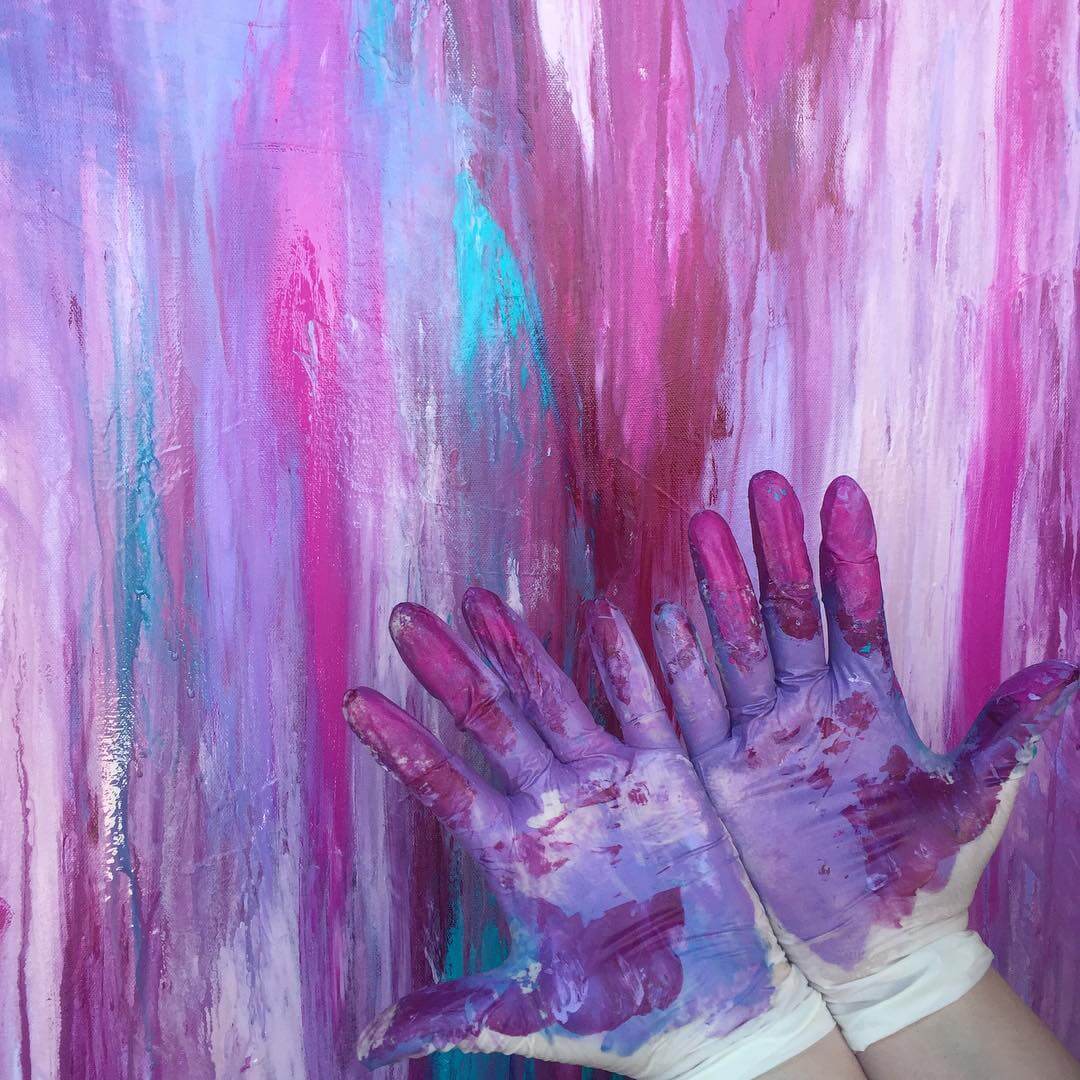 Pauline's two hands in front of an abstract purple painting. Wearing white gloves, her hands are covered in paint.