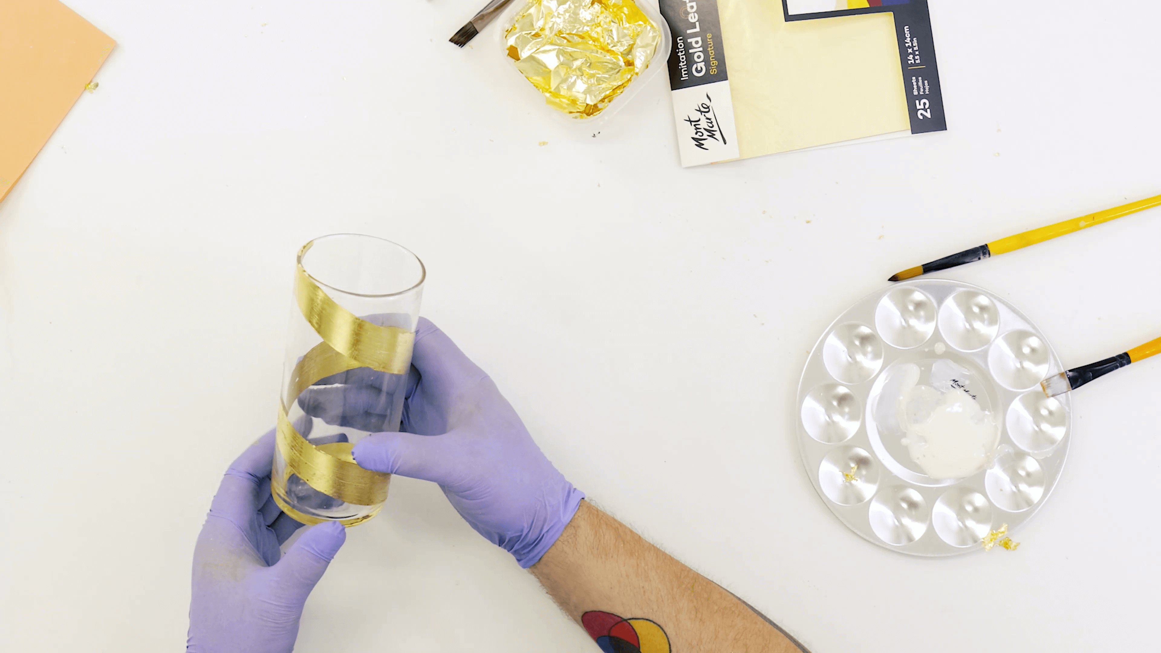 Person wrapping gold leaf on a glass cup, with purple gloves on.