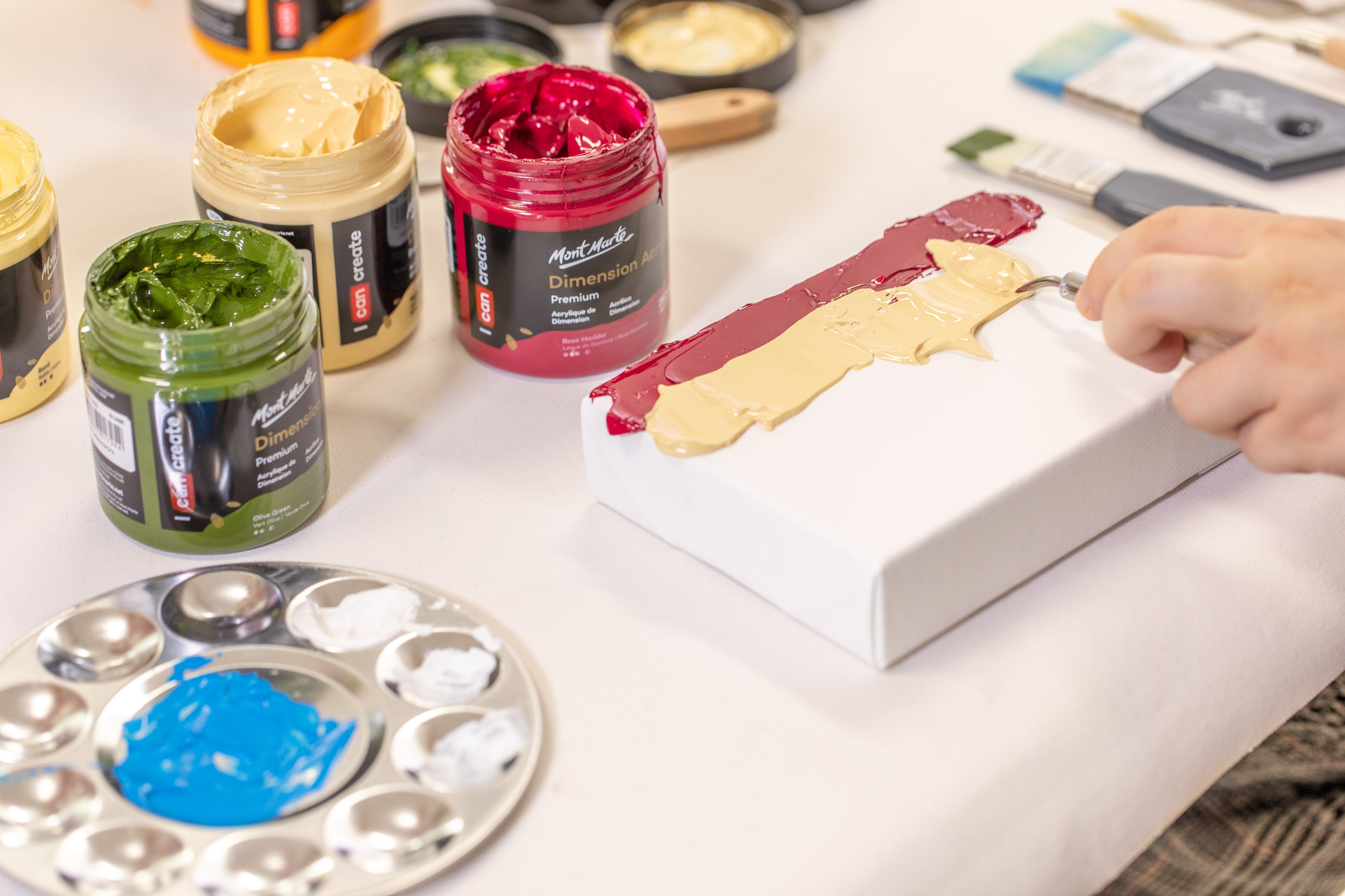 2. Red and sand coloured Dimension Acrylic paints being applied with a palette knife onto a canvas