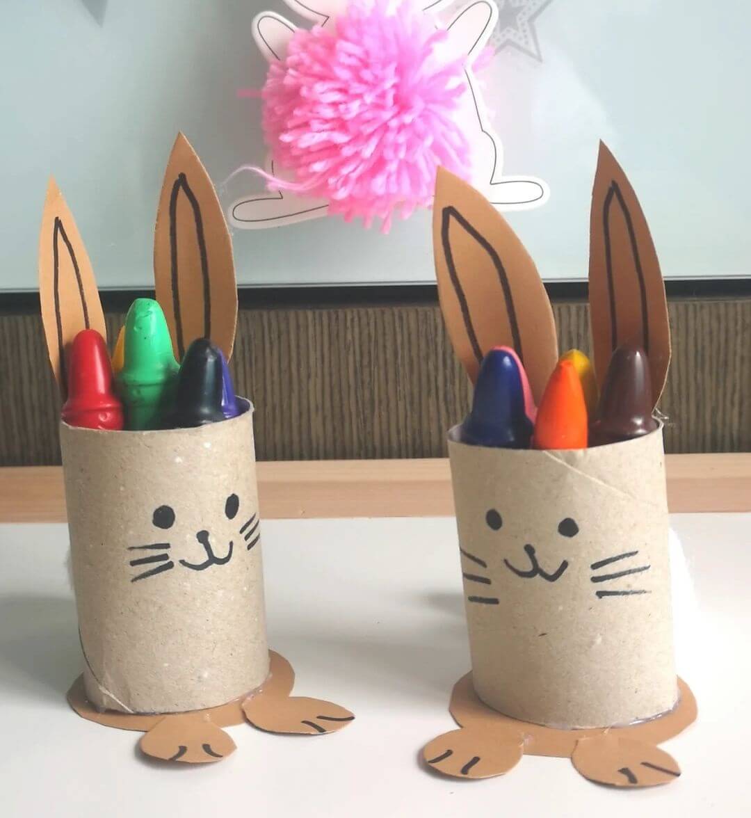 Two Easter bunny crayon holders made from cardboard and a cardboard roll, with crayons inside.