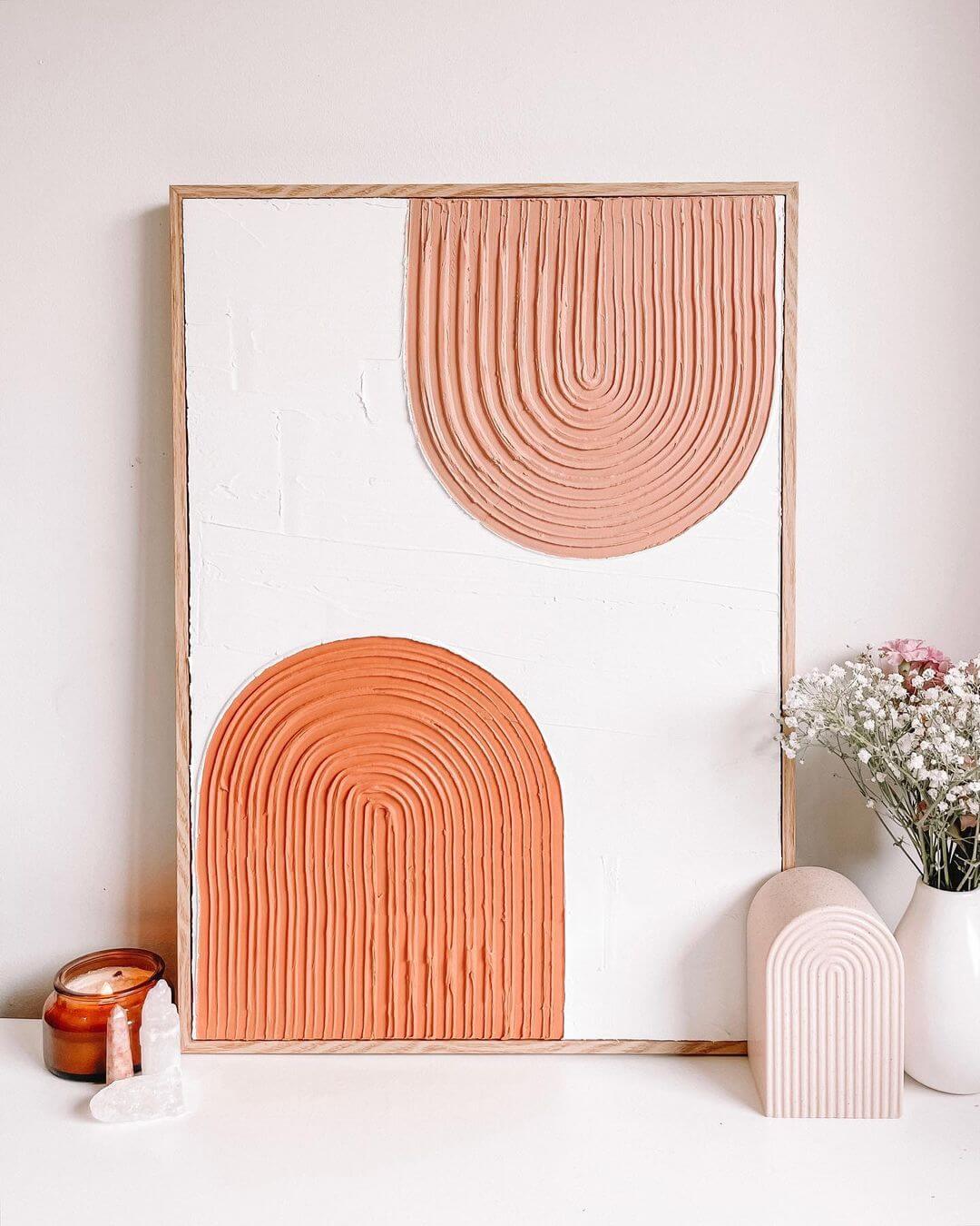 Two geometric arches painted in coral and terracotta next to a vase of dried flowers and a candle.