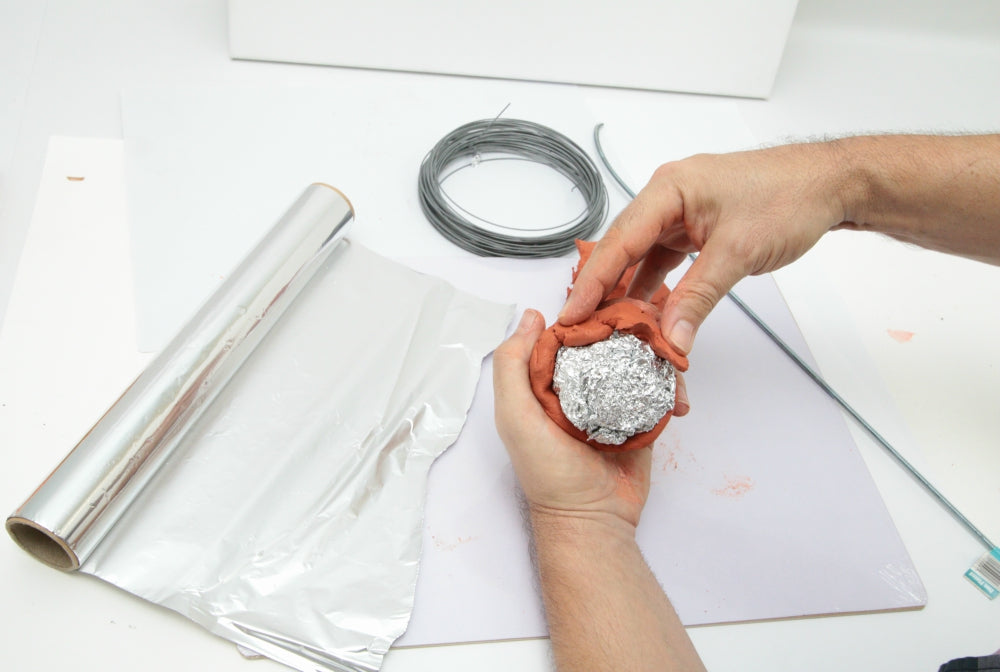 Hands using aluminium foil to create an armature and bulk the clay work.
