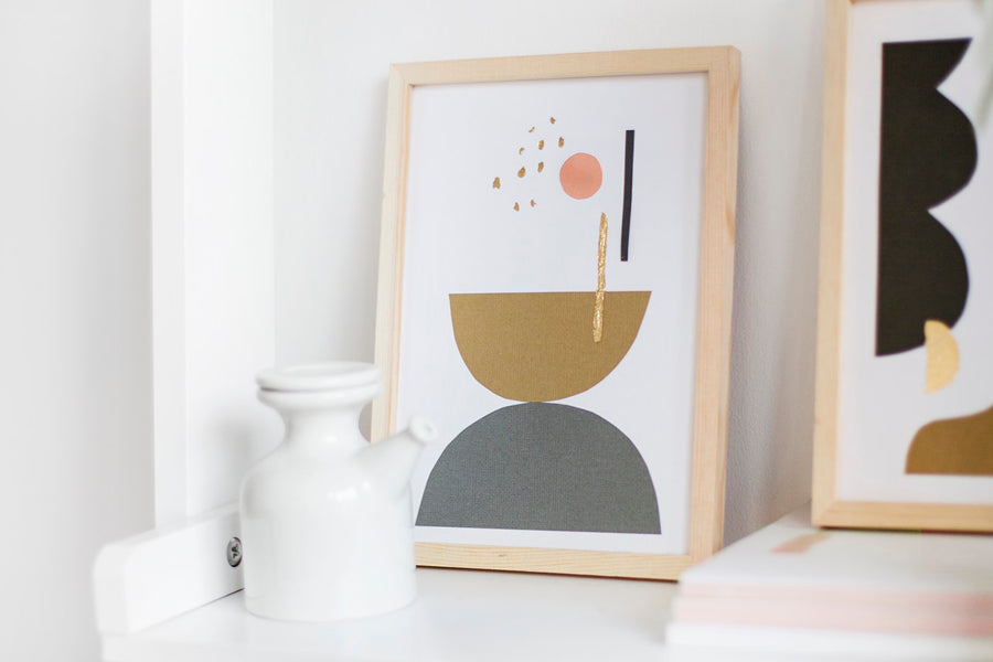A geometric canvas in a wooden frame, next to a white vase.