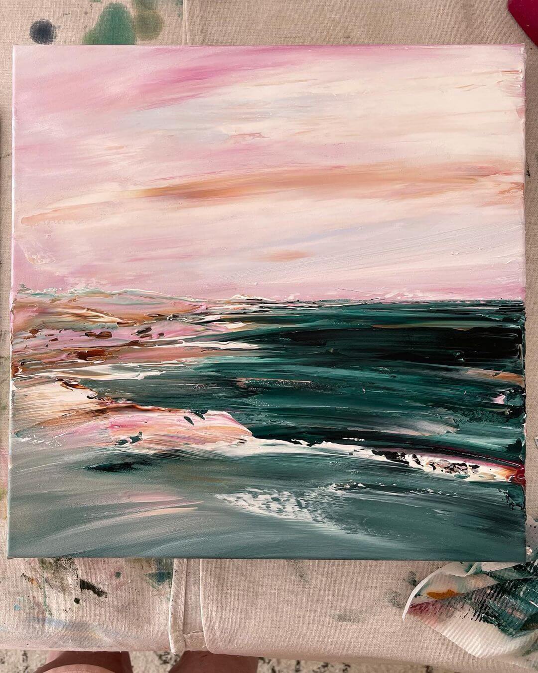 3. A pink sunset seascape artwork made with palette knives sitting on a table with paper towel next to it.