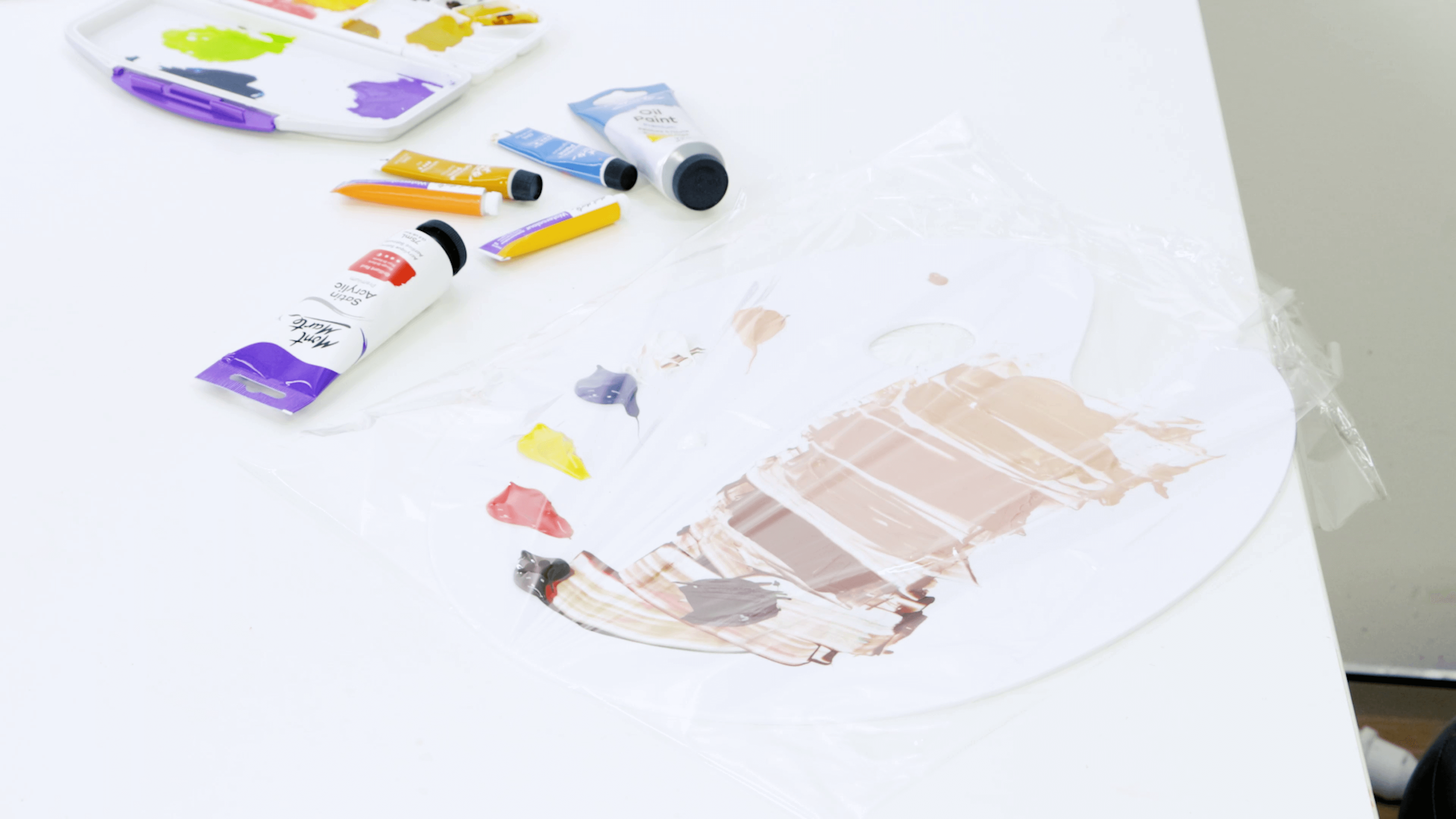 A used paint palette with acrylic paint on it, covered in cling wrap to store the palette.