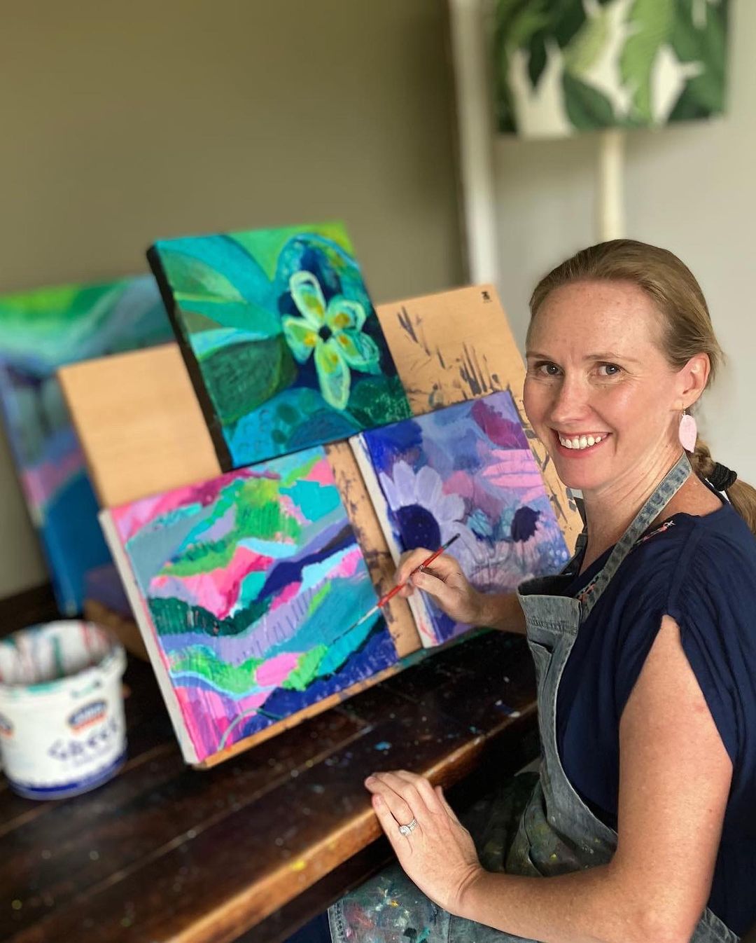 3. Amy compton sitting in front of 3 paintings propped on a board