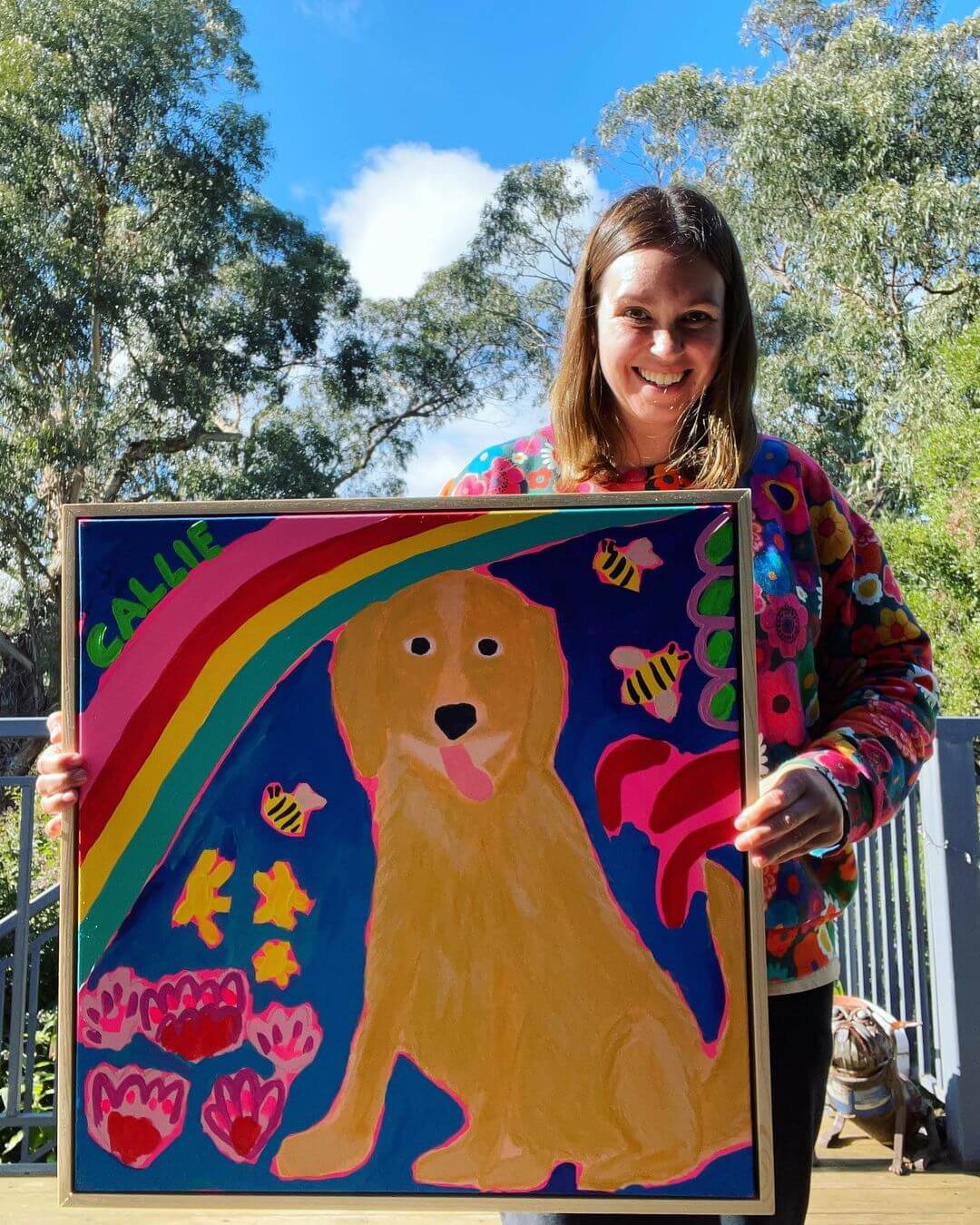 Artist Emily Viski smiling and holding an artwork of a dog drawn in an abstract, cartoon style.