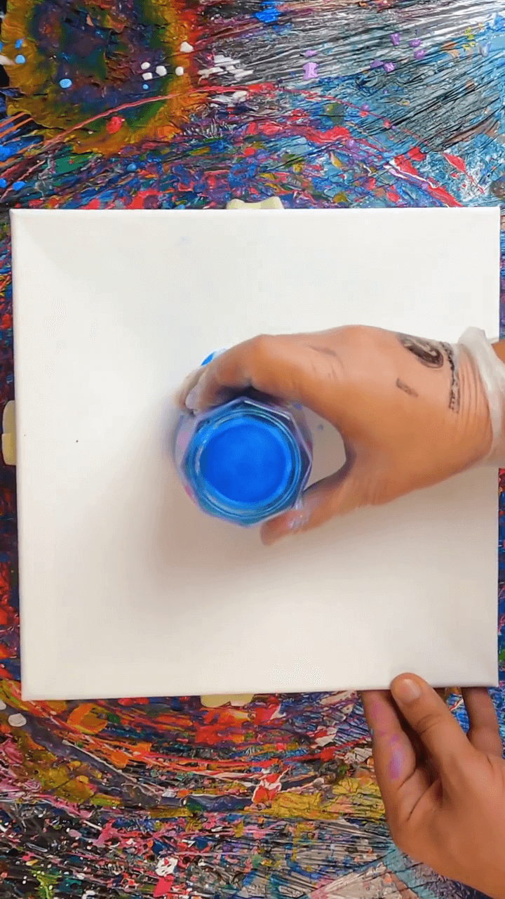 3. Artist Mr Goodriddance holding a cup of blue pour paint onto a white canvas for a flip cup pour technique.