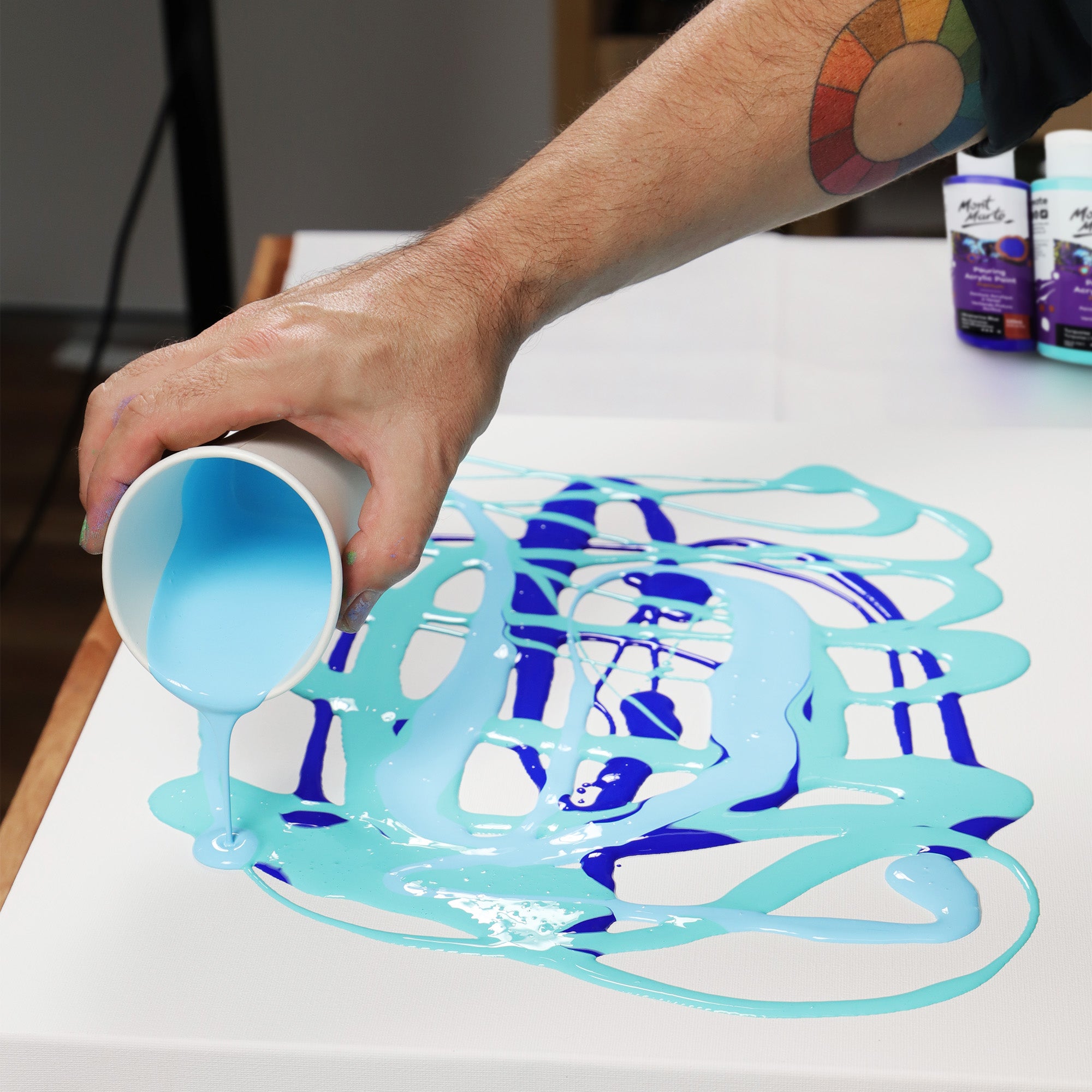 3. Blue acrylic paints being poured onto a fluid canvas