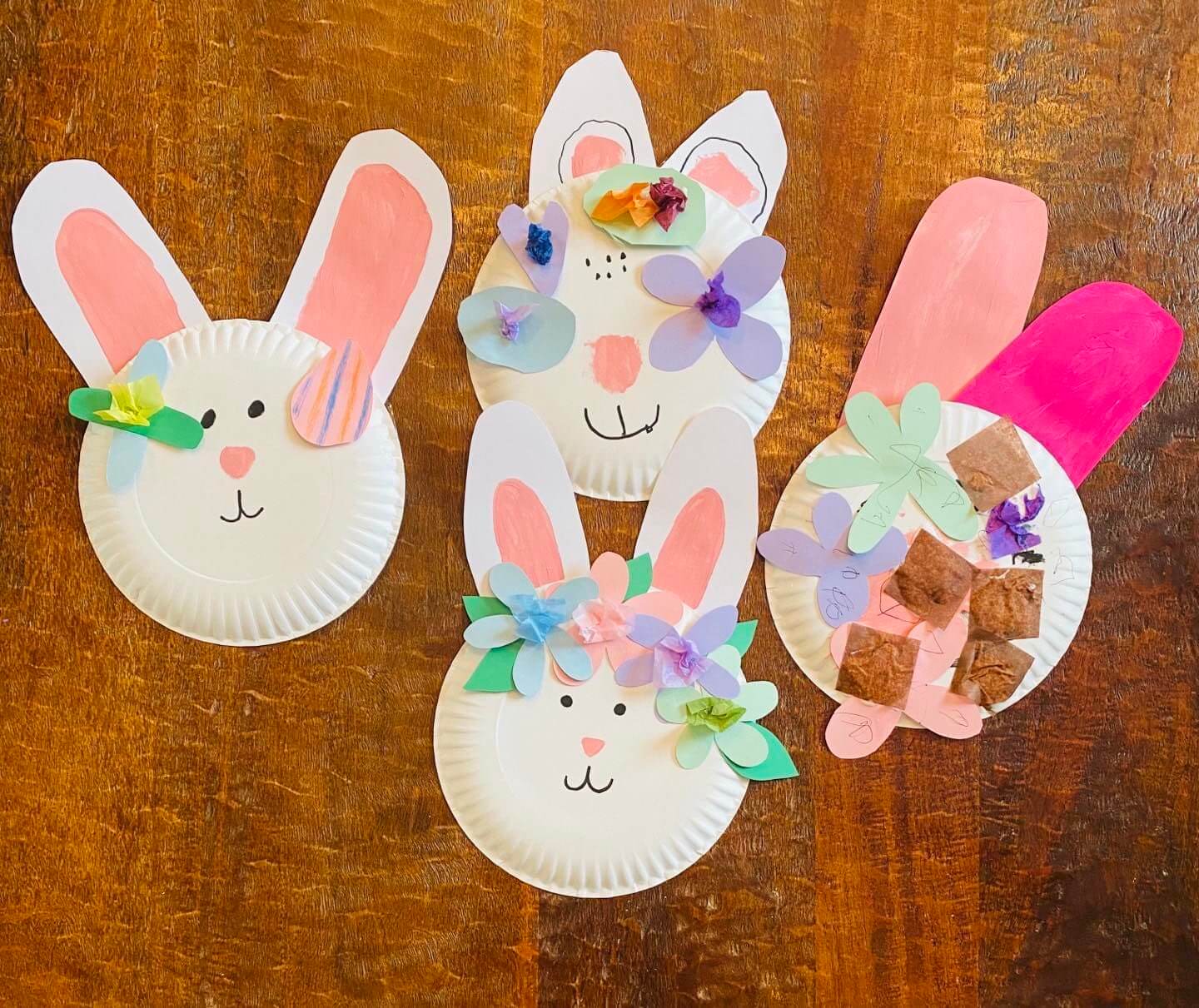 Four paper plates decorated with Easter Bunny faces on them, laying on a wooden table.