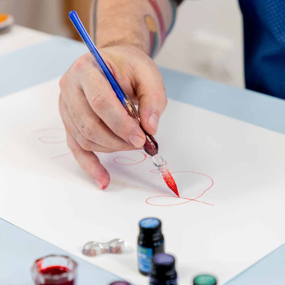 Hand holding a glass dipper pen and writing create on white paper