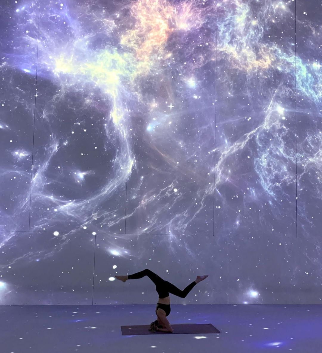 Jenna doing yoga in an open space with a galaxy projected on area