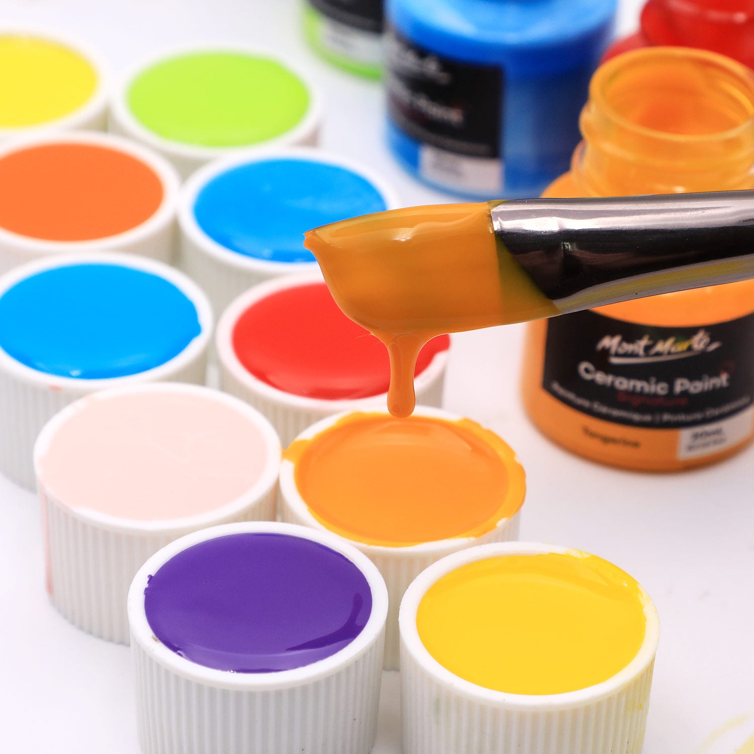 3. Mont Marte Ceramic Paints poured into their caps, with a paintbrush dipped into the orange paint and dripping