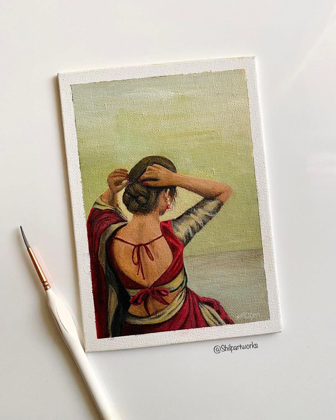 3. Painting of a woman in red tying up her hair, artwork is next to a white brush.