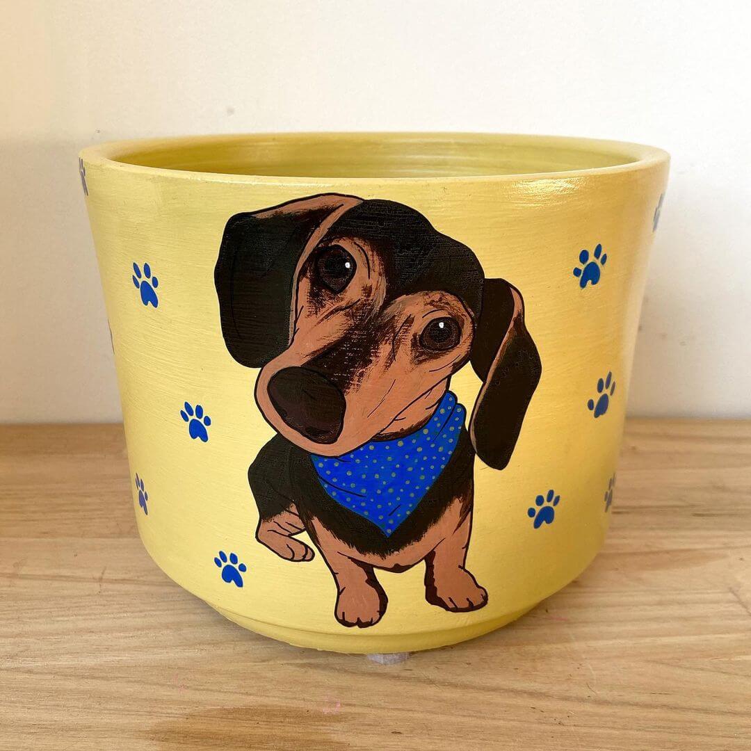 Pastel yellow pot plant with realistic dachshund painted on top with small blue paw prints painted on.