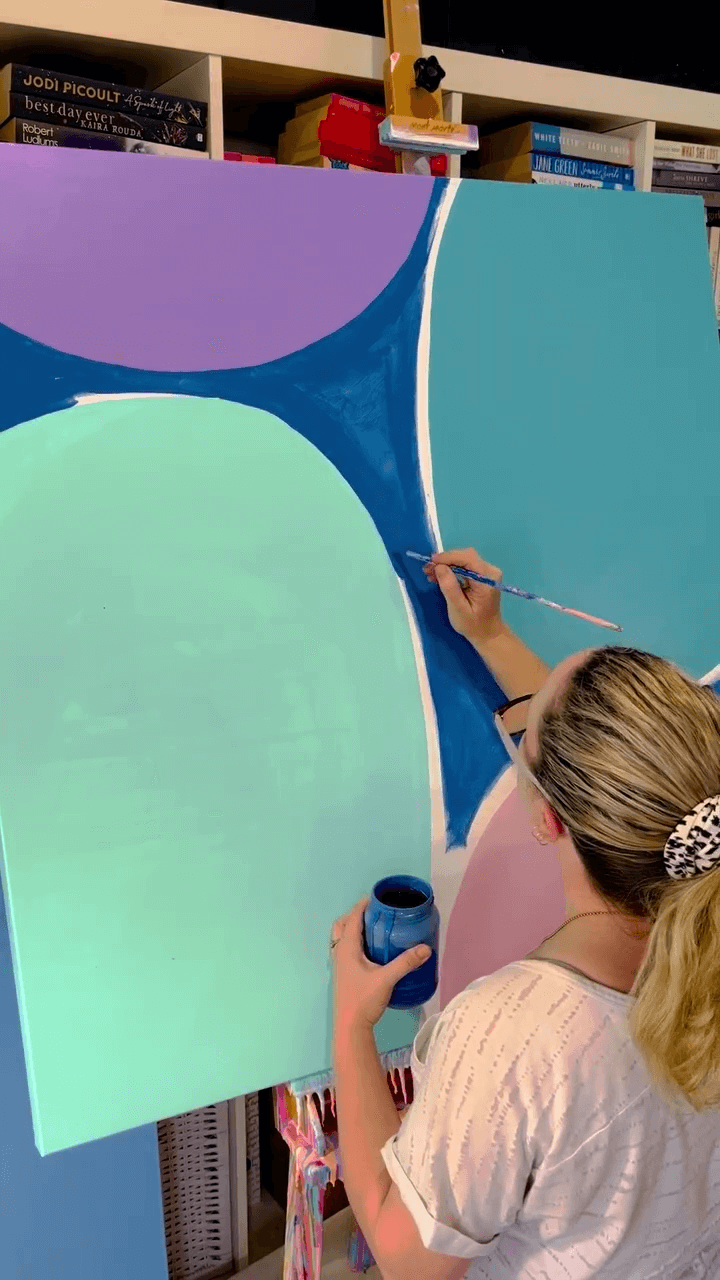 3. Poppy Key painting a blue abstract artwork with various blue shapes on the canvas.