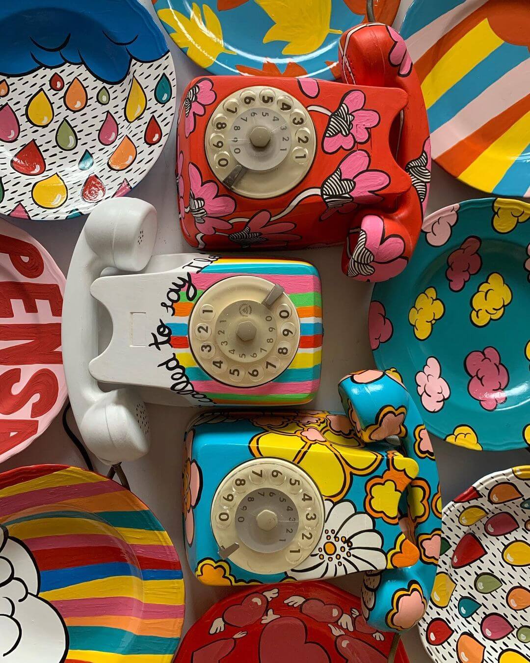 Three vintage telephones painted in a pop-art style next to seven upcycled ceramic paints too.