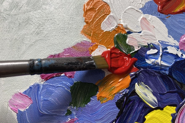 Close up of paint brush adding red paint to an expressionist style painting of a vase of flowers.  