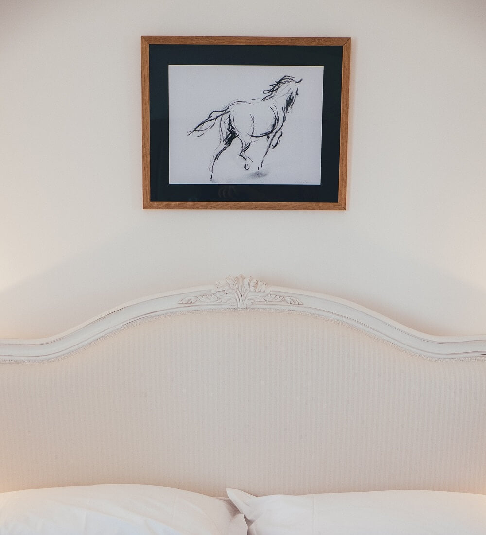 Charcoal drawing of a horse hanging in a frame above bed. 