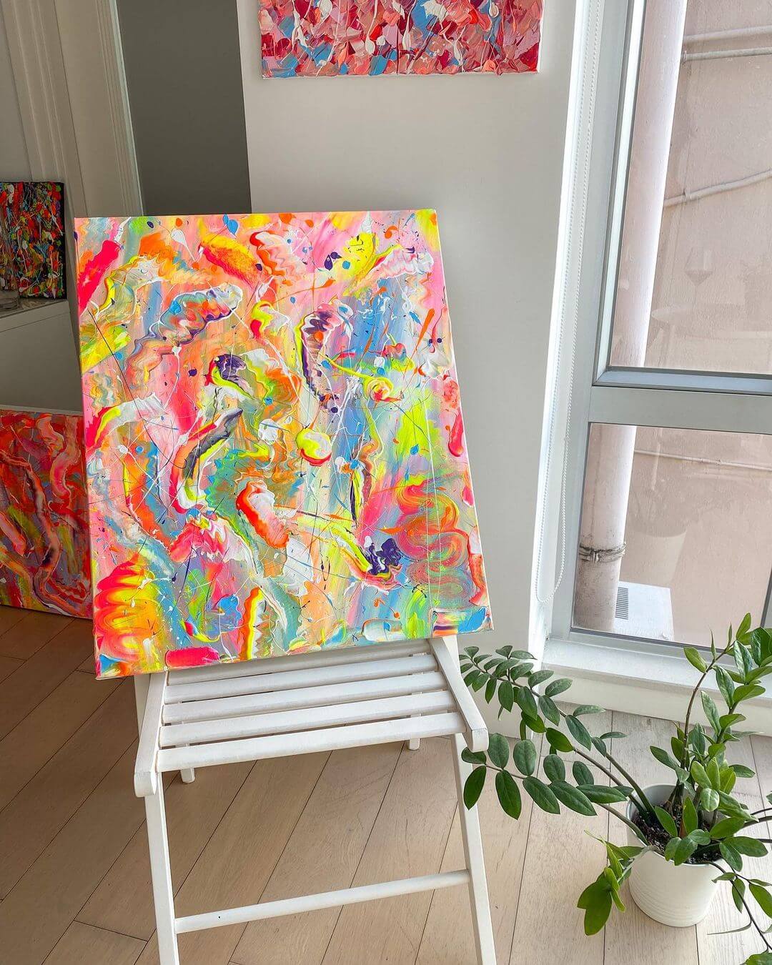 A coloured abstract painting on a white wooden chair with a green plant next to it