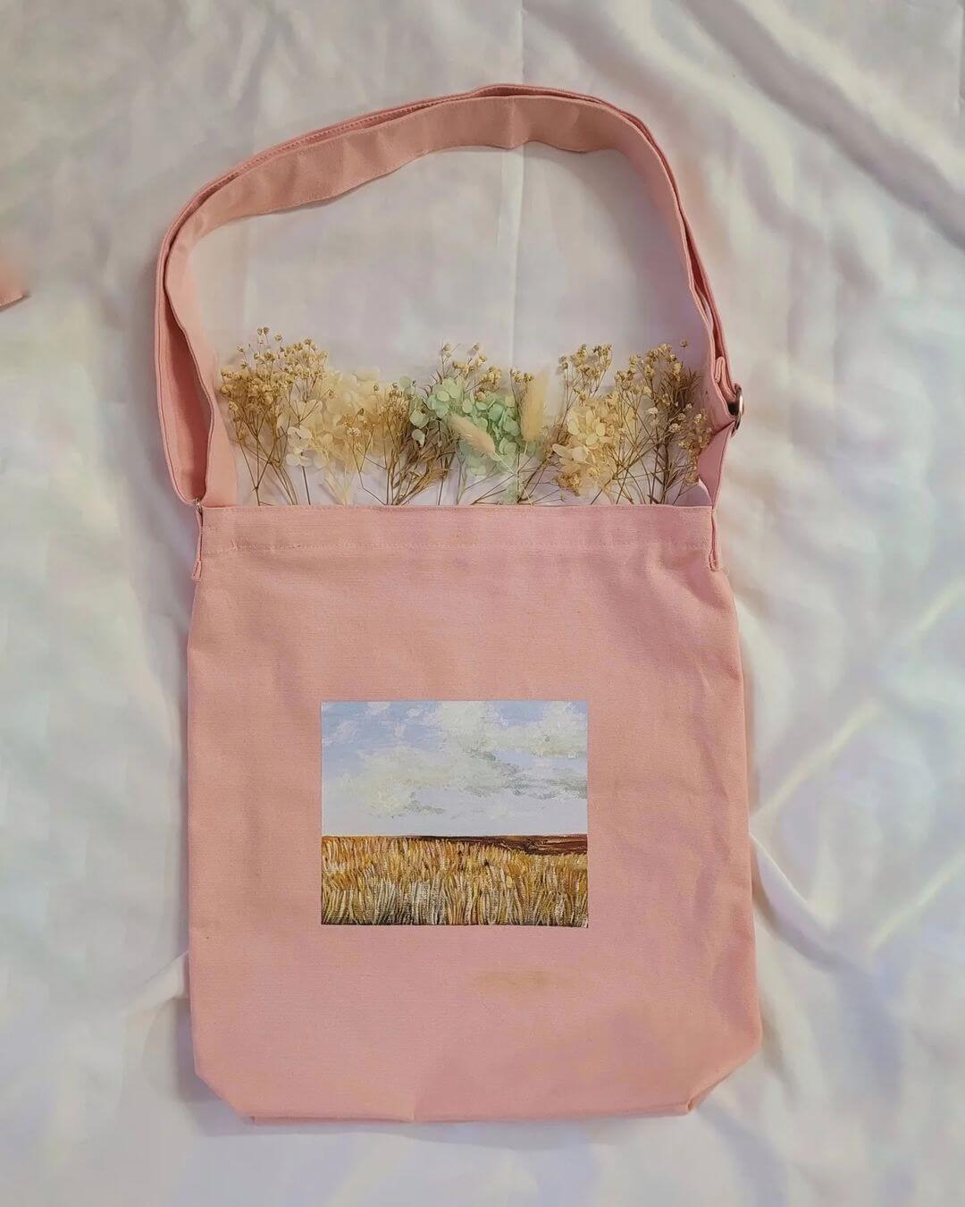 4. A pink tote bag with a painted flower field on it, with dried flowers inside the bag.