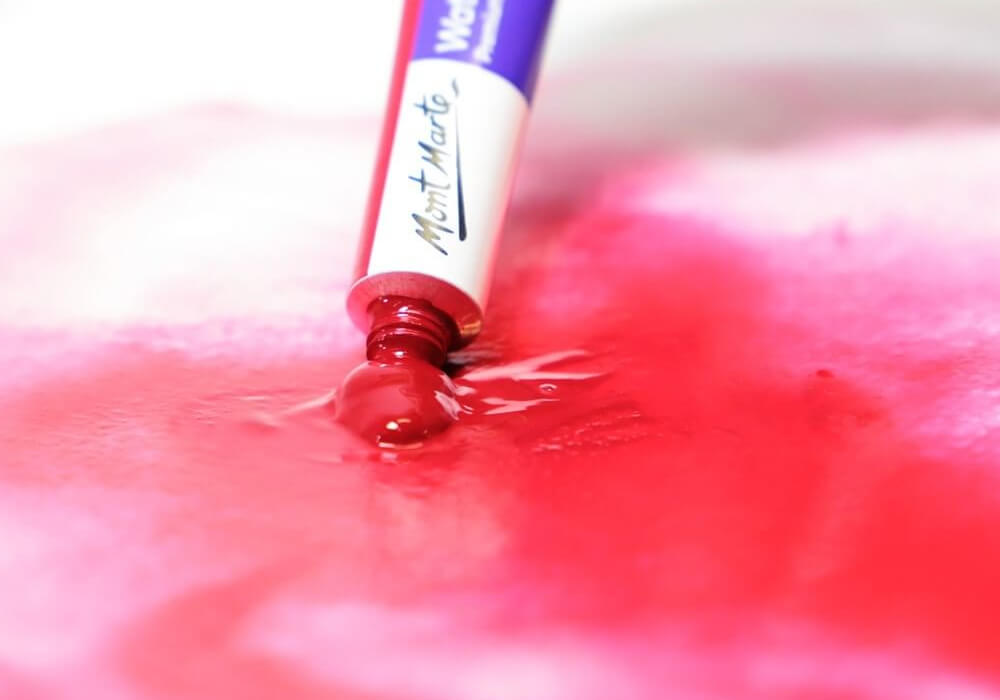 A red watercolour tube being squeezed out onto paper.