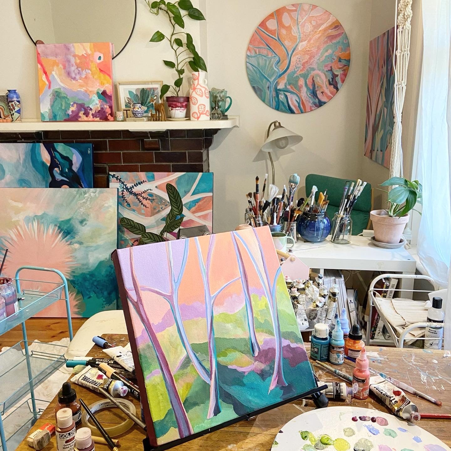 Abstract rainforest paintings in Tessa's creative studio next to a pastel blue trolley with paints, brushes and accessories on a table nearby.