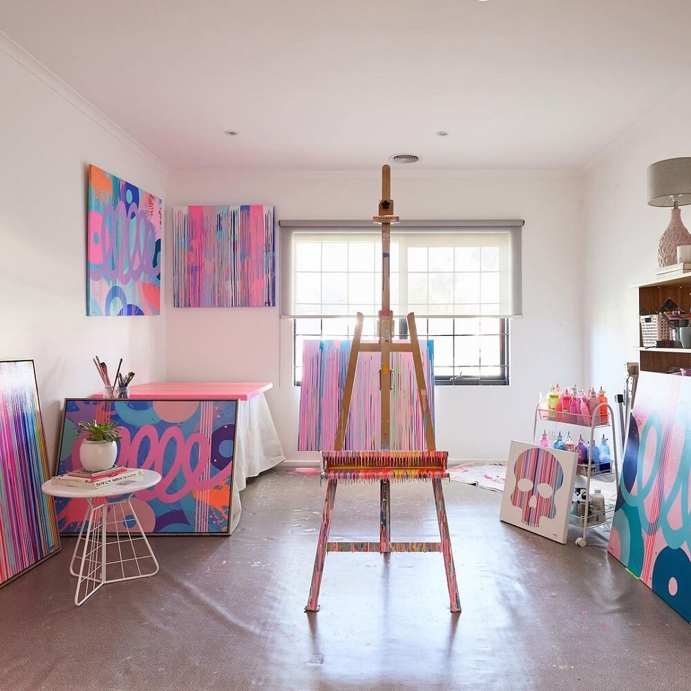 An empty easel stands in a studio with bright abstract canvases.