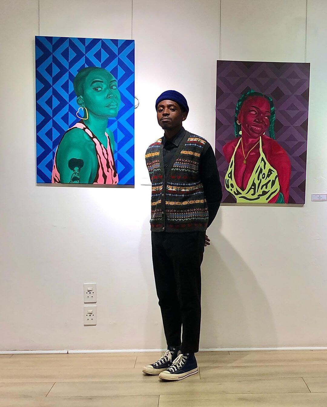 Artist Jason Langa standing in front of two bright oil paint portraits.