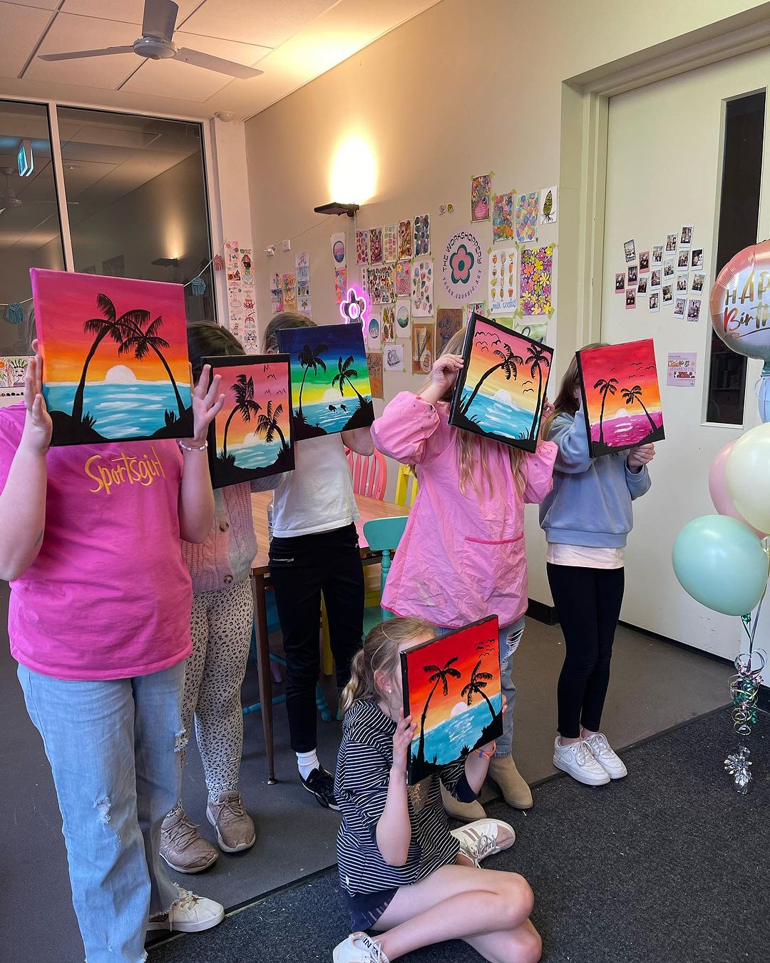 4. Class of workshop attendees holding sunset beach paintings in front of their faces