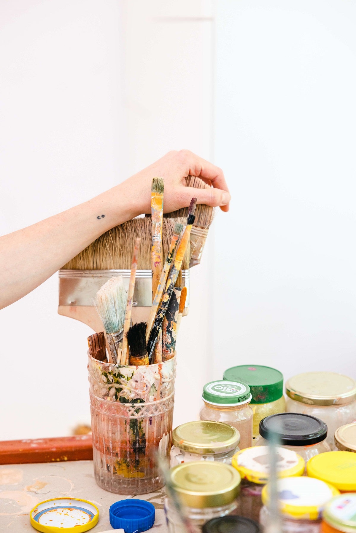 Empty glass jars next to a jar of used paint brushes with a hand holding the bristles.